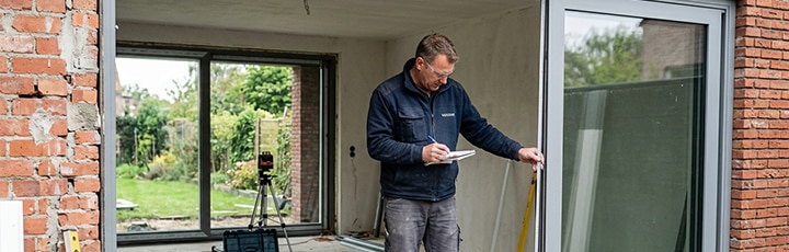 Vakman bezig met inmeten van kozijnen en ramen aan een woning